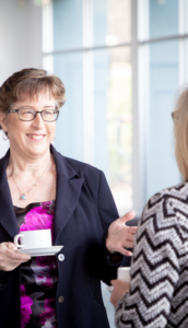 Carolyn Jeffery holding a teacup, chatting with a network member.