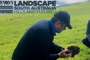 Farmer holding a handful of soil in a grassy field.