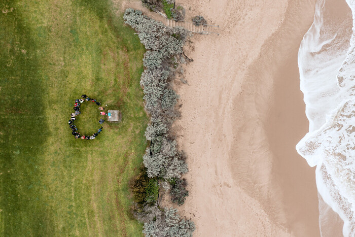 Drone arial shot of 2023 program participants standing in a circle near the shore