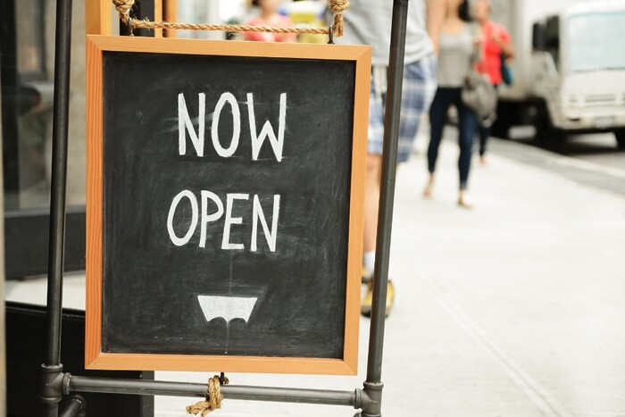 Chalk board on streetside with "NOW OPEN" written on it.